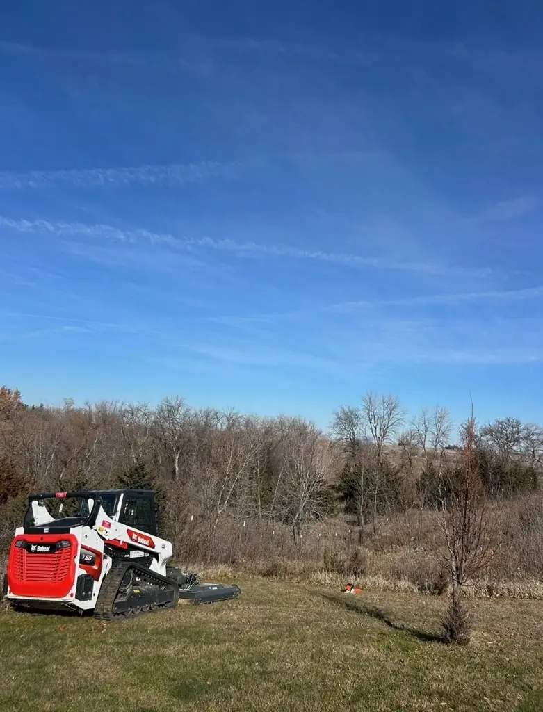 Skid steer mowing rough grass on open acreage