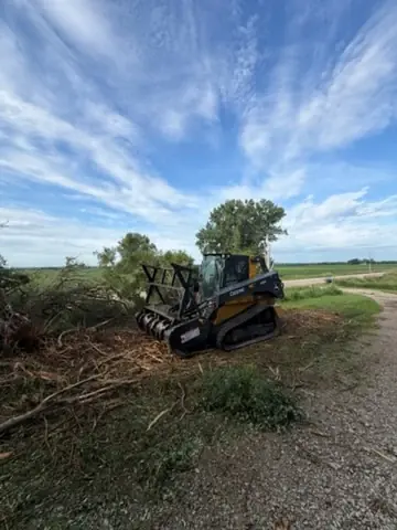 John Deere skid steer with a mulching head beside a brush pile